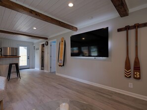 Ein geräumiger Raum mit Holzbalkendecke, einem großen Flachbildfernseher an der Wand und zwei Holzschlägern, die an der Wand hängen.