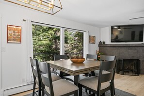 Een eethoek met een tafel, stoelen, een open haard en een aan de muur bevestigde televisie.