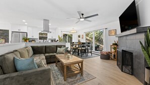 Ein modernes Wohnzimmer mit einem Ecksofa, einem Essbereich, einem Kamin und einer Küche im Hintergrund.