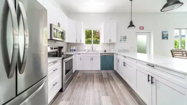 A modern kitchen with white cabinets, stainless steel appliances, and a wooden floor.