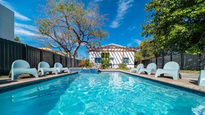 A swimming pool with white lounge chairs, a wooden fence, and a building with a green sign.