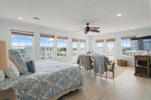 Une chambre spacieuse avec un grand lit, un ventilateur de plafond et un balcon offrant une vue agréable.