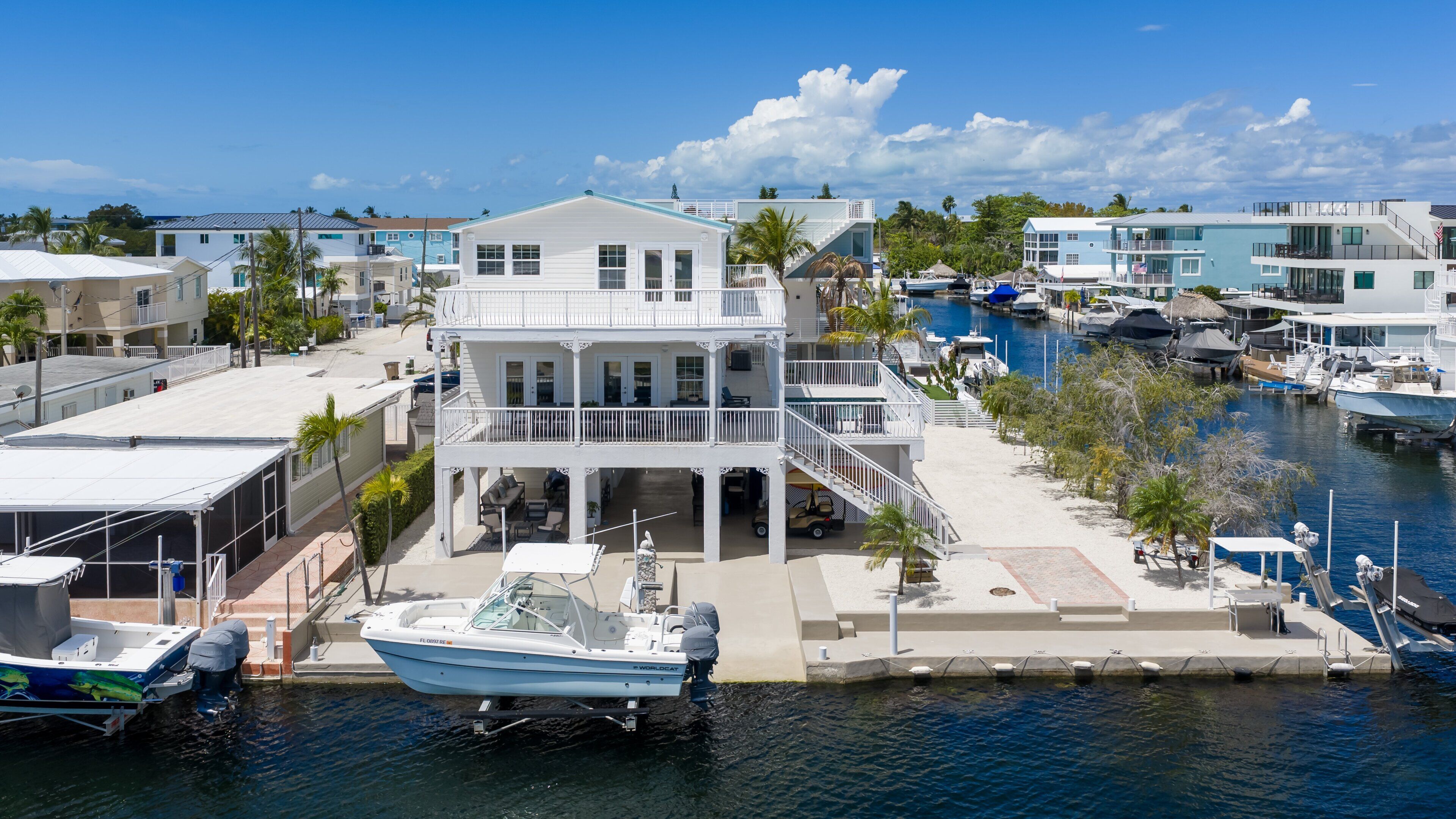 Une propriété située au bord de l’eau, avec une grande maison dotée de nombreux balcons, un quai avec un bateau et une marina abritant plusieurs embarcations.