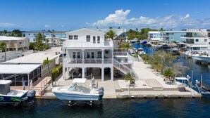 A waterfront property with a large house featuring multiple balconies, a dock with a boat, and a marina with several boats. - Dolphin Paradise: Pool, Elevator, Waterfront with Dock (Key Largo)