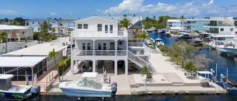 Une propriété située au bord de l’eau, avec une grande maison dotée de nombreux balcons, un quai avec un bateau et une marina abritant plusieurs embarcations.
