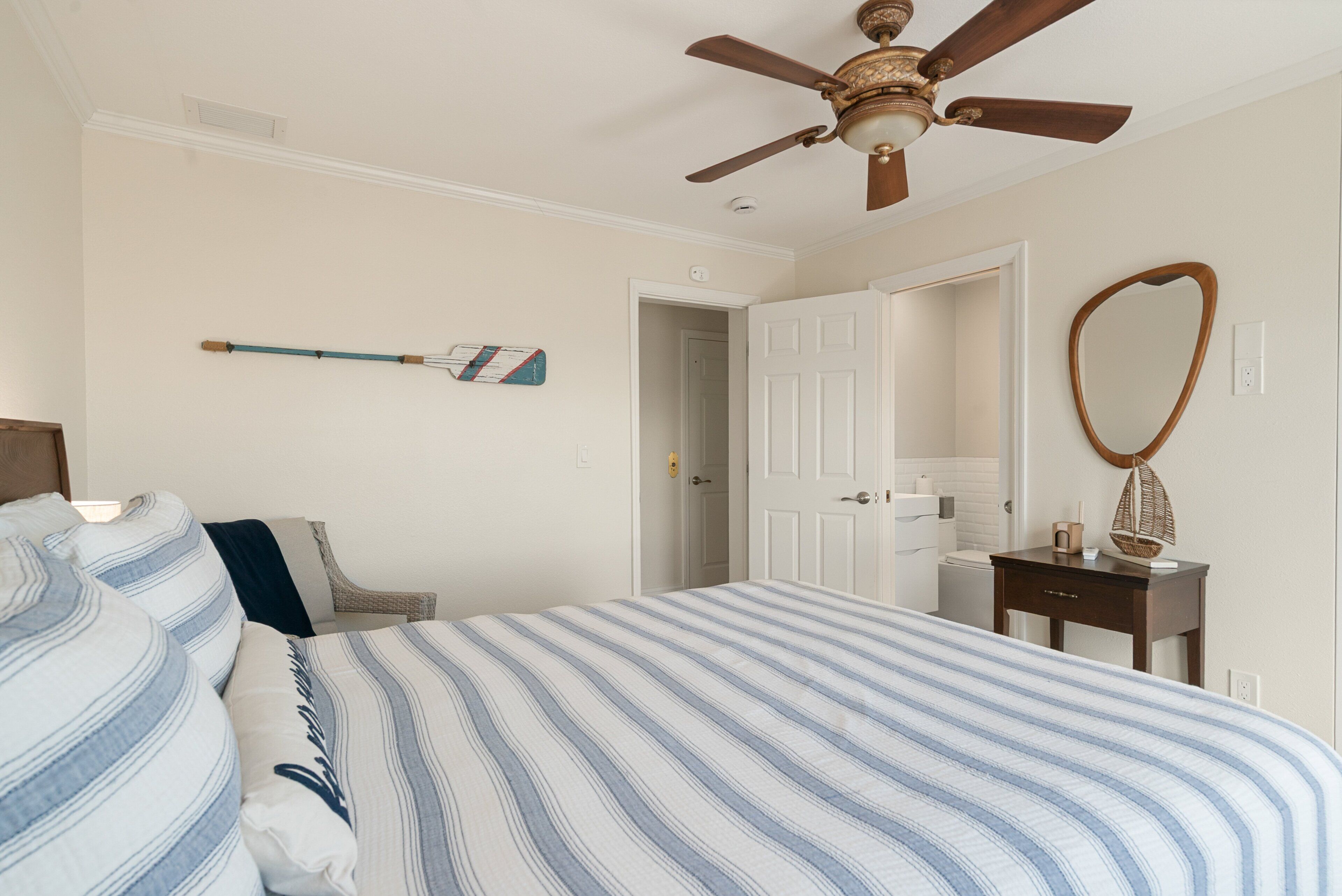 Een slaapkamer met een bed, een plafondventilator, een deur, een spiegel en een nachtkastje.