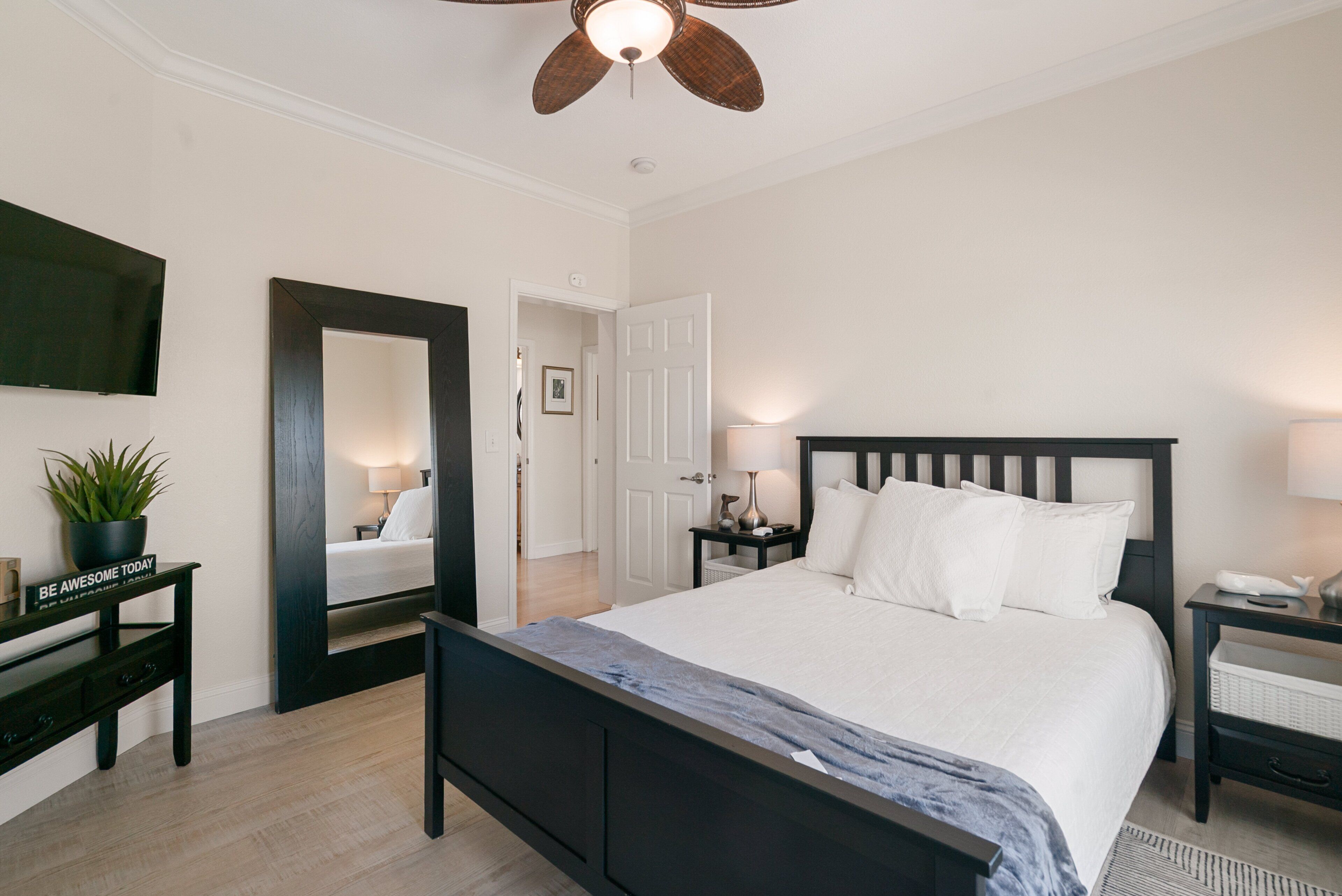 A bedroom with a bed, bedside tables, a mirror, a ceiling fan, and a television.