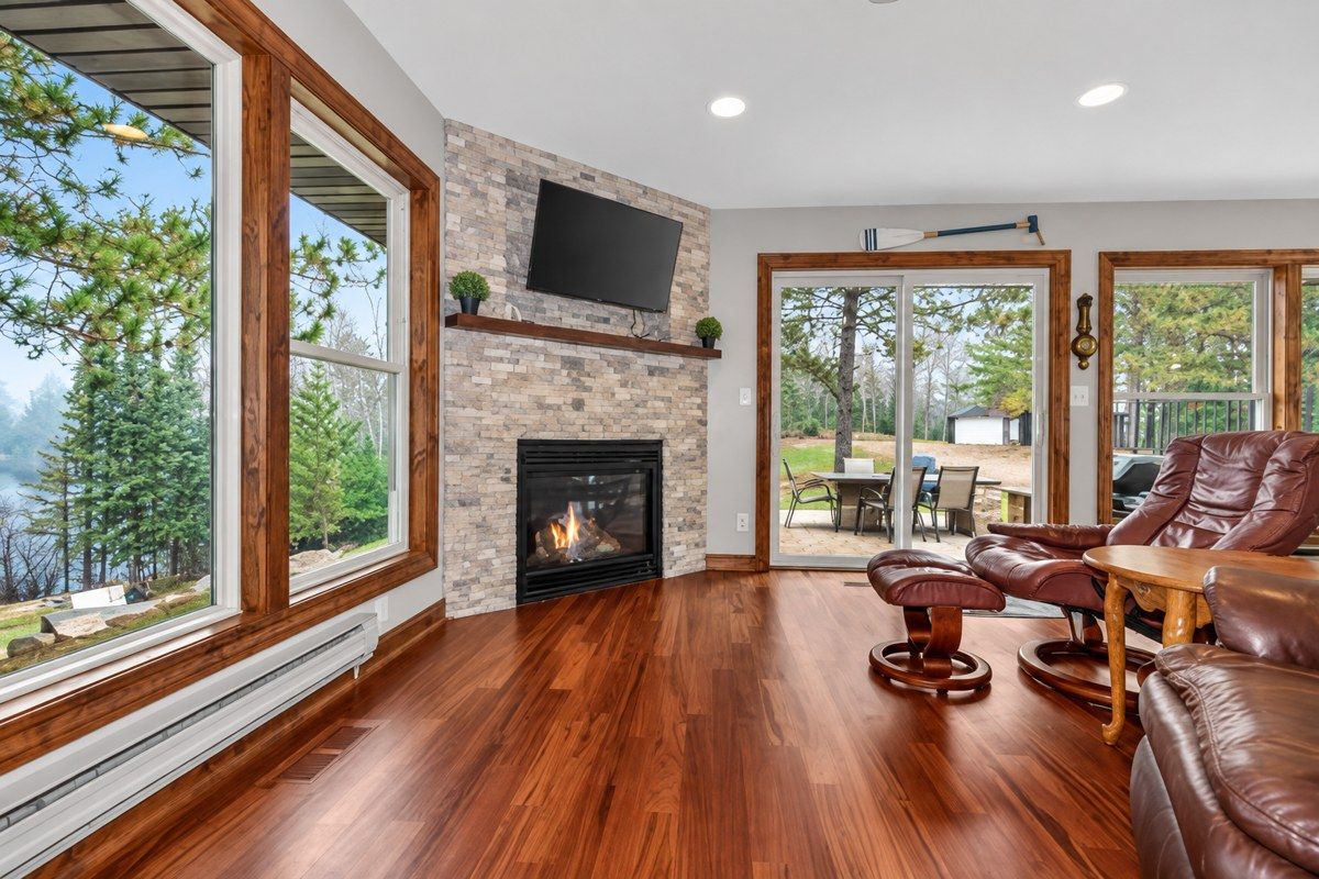 A room with a fireplace, leather seating, and large windows overlooking a forest.