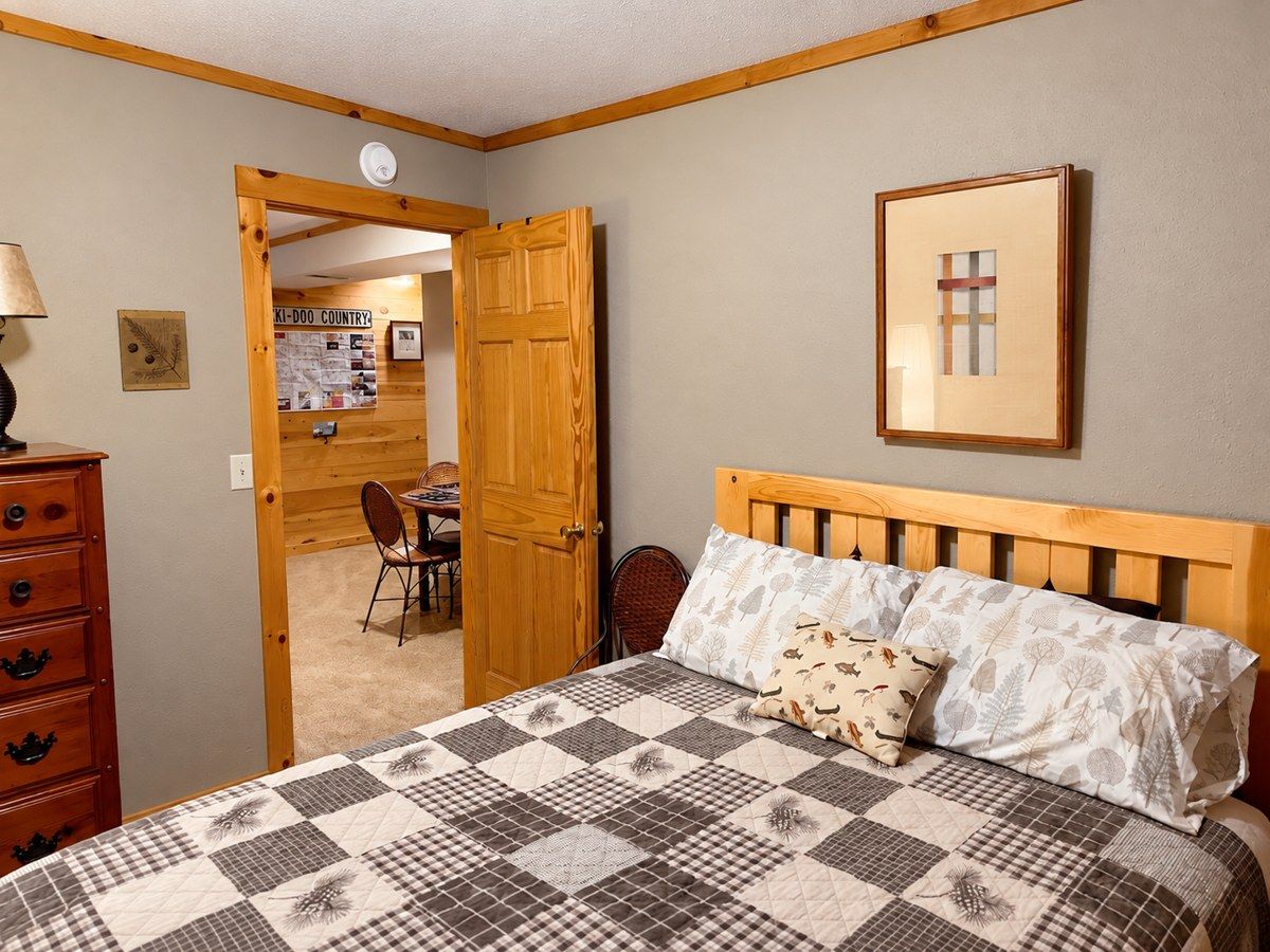 Un dormitorio con una cama de madera, un aparador, una puerta que da a un comedor y un cuadro en la pared.