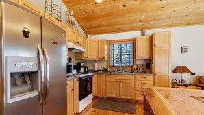 Una cocina con armarios de madera, un refrigerador de acero inoxidable, un horno y una ventana con vista a árboles.