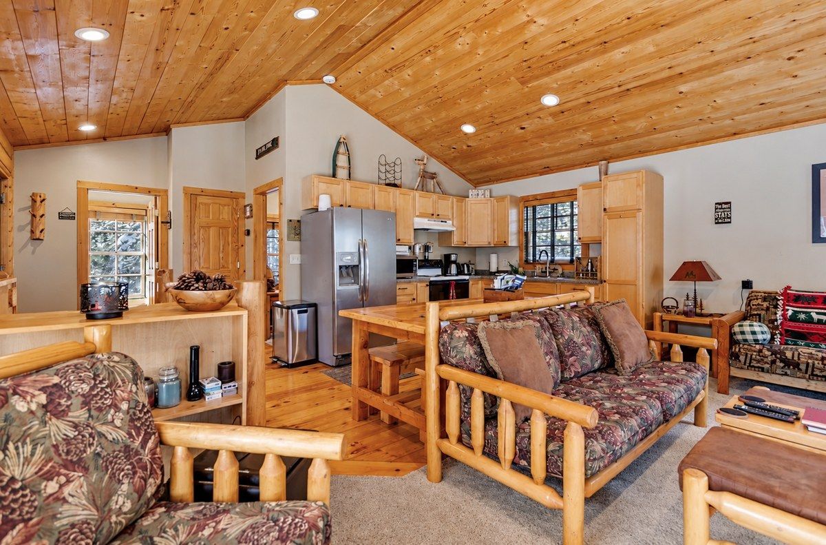 Interior acogedor de una cabaña con una mesa de comedor de madera, un sofá y una cocina con armarios de madera y un refrigerador.