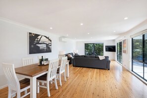 Ein modernes Wohnzimmer mit einem Holzesstisch, weißen Stühlen, einem grauen Sofa und einem großen Fenster.
