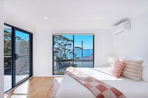Ein Schlafzimmer mit großem Fenster, einem Bett, einem Nachttisch und einer Wand-Klimaanlage.