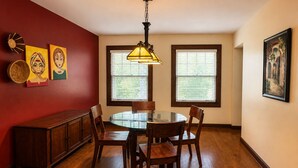 Een eetkamer met een ronde glazen tafel, houten stoelen, een houten kast en een hanglamp.