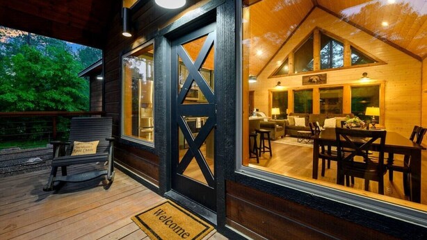 Una baita di legno con un portico, un tappetino d'ingresso, una panchina e un'area pranzo con tavolo e sedie.