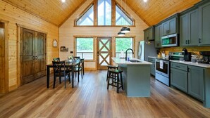 Interno di una baita di legno con zona pranzo, cucina e ampie finestre.