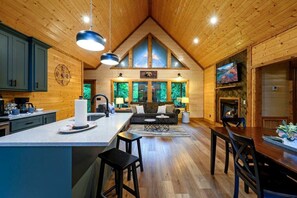 Ein Holzblockhaus-Interieur mit Küche, Essbereich und Wohnzimmer, mit Holzwänden, einem Kamin und großen Fenstern.
