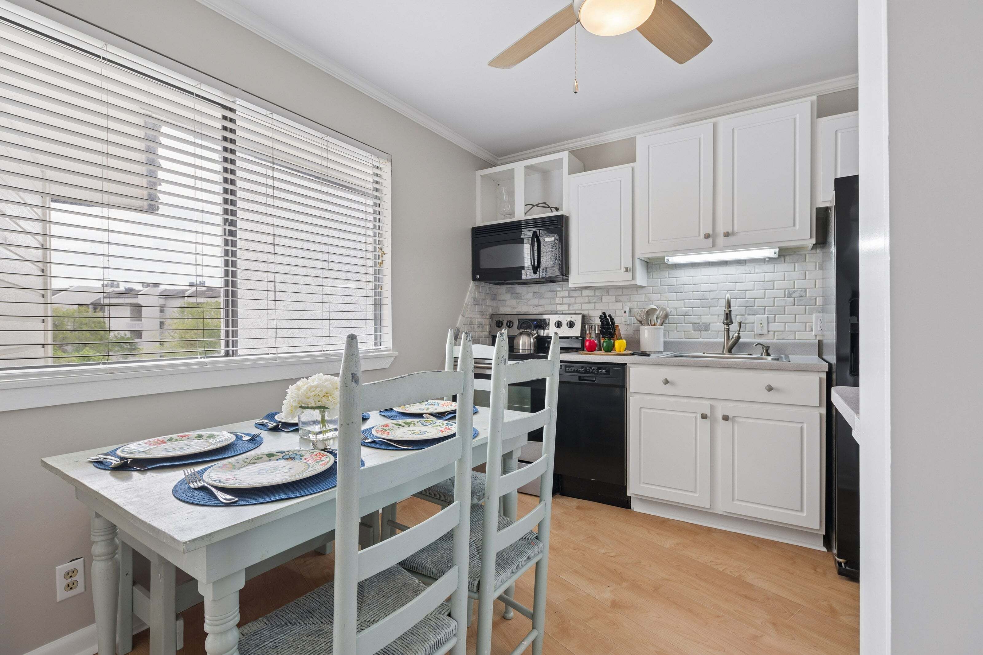 A kitchen with white cabinets, a microwave, a dishwasher, and a dining table set with plates and cutlery.