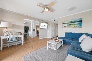 Una sala de estar moderna con un sofá azul, una mesa de centro blanca y un comedor con una mesa y una silla blancas.