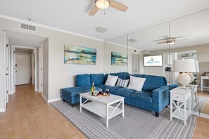 A living room with a blue sectional sofa, a white coffee table, and a TV mounted on the wall. - Beach Resort Stay | Ocean Views, Pool, Bunk Beds, Sleeps 7, Walkable to Coligny Plaza! (Hilton Head Island)