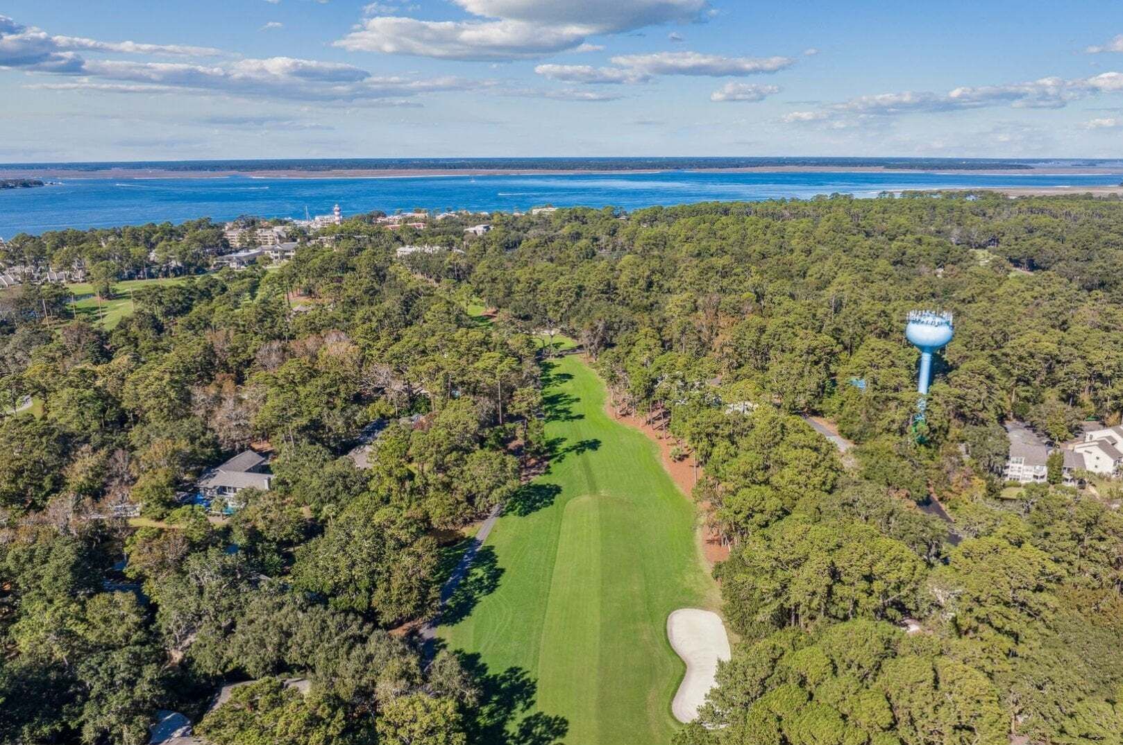Vista aérea de un campo de golf con un faro, un bosque denso y el mar de fondo.