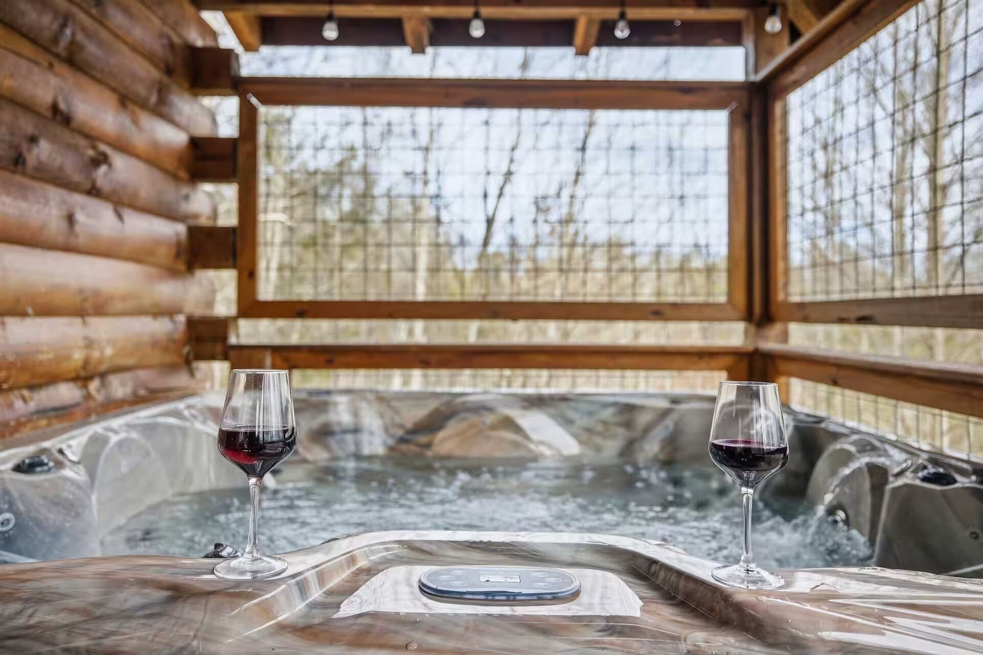 A wooden cabin with a hot tub and two glasses of red wine.