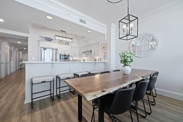 Una cocina moderna con una isla central, iluminación colgante y un comedor con mesa y sillas de madera.