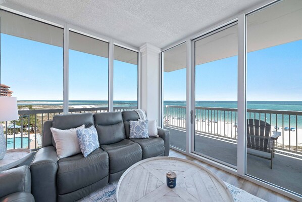 Ein Balkon mit Meerblick, ein graues Sofa mit gemusterten Kissen und ein runder Couchtisch aus Holz.