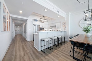 Una cocina moderna con muebles blancos, una isla central con taburetes y un comedor con mesa y sillas de madera.