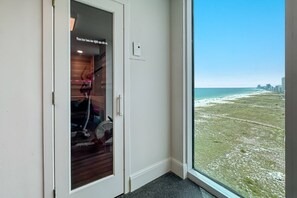 Ein Zimmer mit großem Fenster, einer Tür mit Schild und Blick auf Strand und Stadtlandschaft.