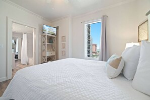 Habitación de hotel con una cama grande, un televisor sobre un mueble, una ventana con vistas a edificios y una puerta que da a un baño.