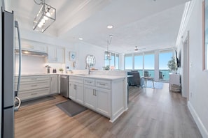 A modern kitchen with white cabinetry, a central island, and a view to the living area. - Perdido Dunes Tower 5 East | New + Gulf-Front (Orange Beach)