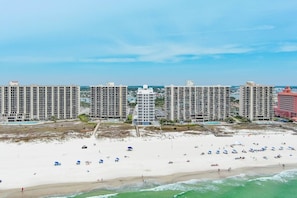 Ein Hotel direkt am Strand mit mehreren hohen Gebäuden, einem Sandstrand und blauem Himmel.