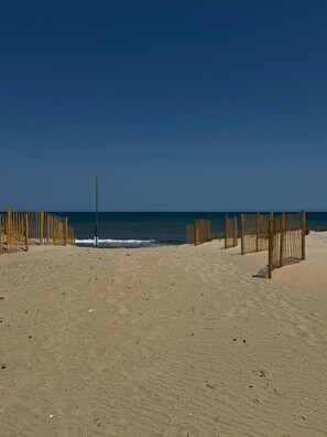 Een zandstrand met houten omheiningen en een helderblauwe lucht.