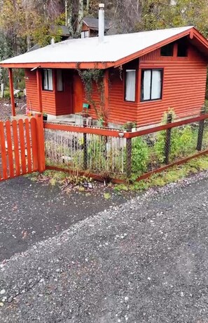 Une cabane en bois rouge avec un porche, une cour clôturée et une allée en gravier.