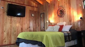 A wooden cabin-style room with a bed, a television, and a wall-mounted light fixture.