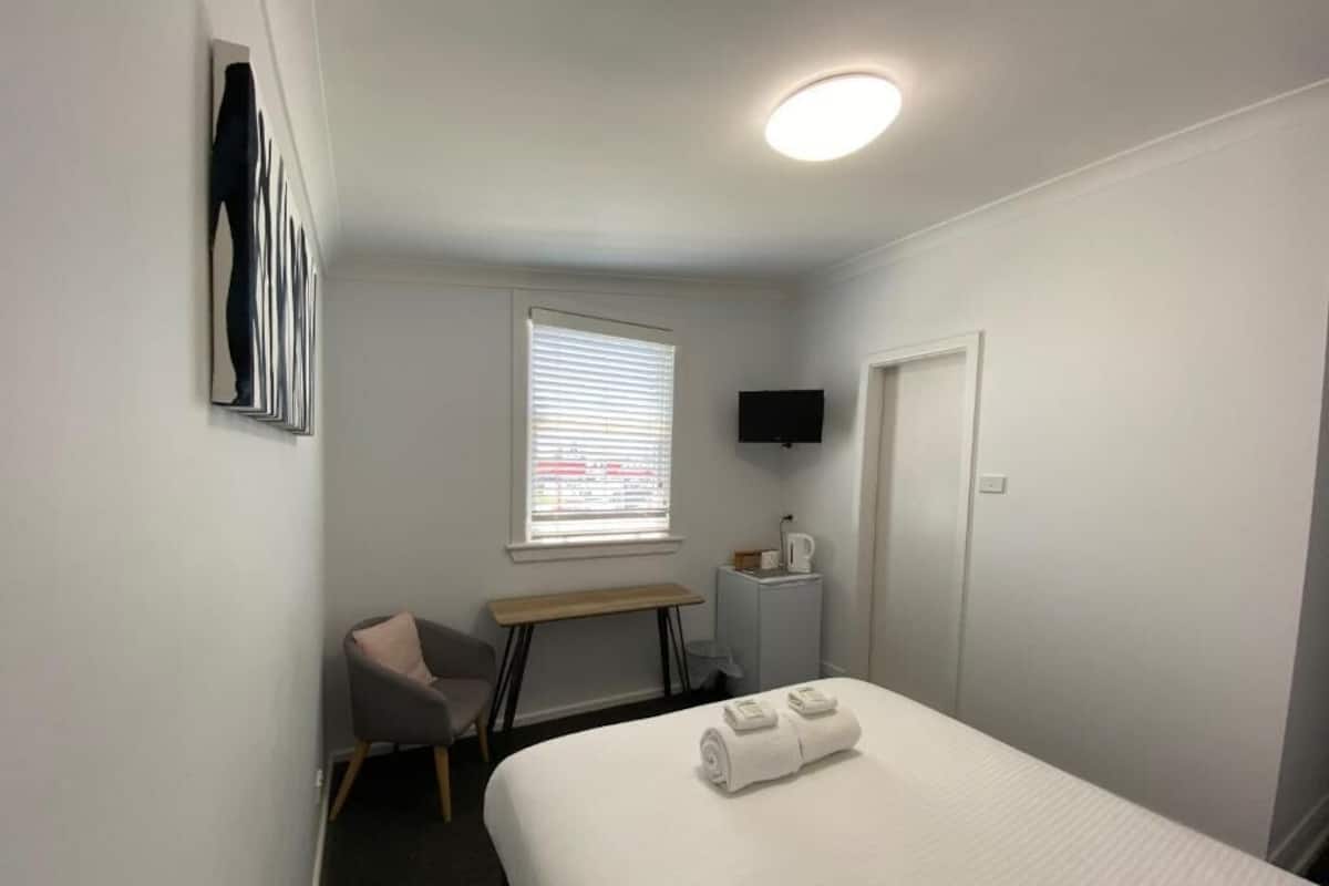 Une chambre d’hôtel avec un lit, un bureau, une chaise, une télévision et une fenêtre.