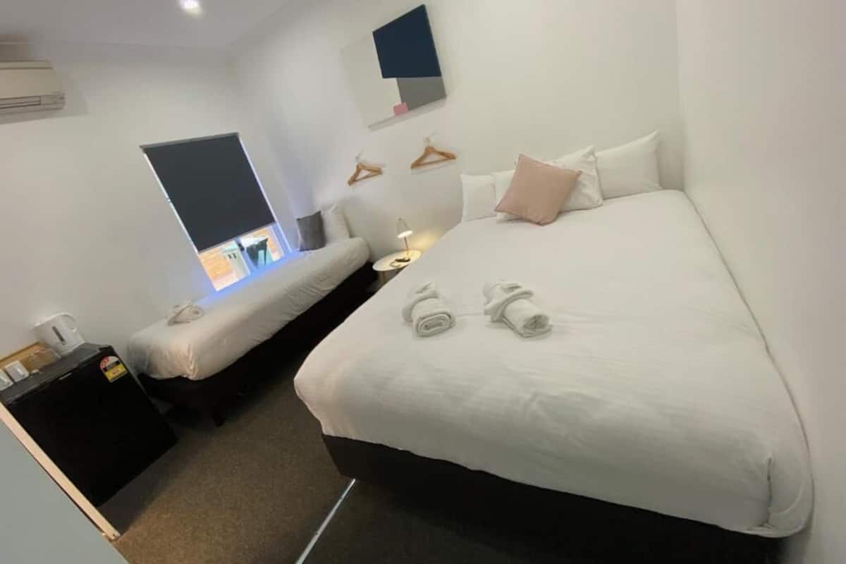 Une chambre d’hôtel avec un grand lit, un lit plus petit, un bureau avec une lampe et un téléviseur fixé au mur.