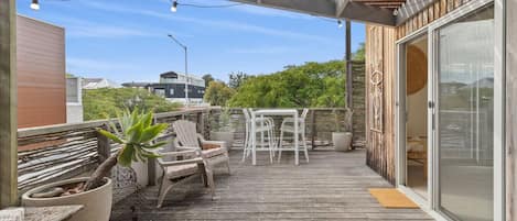 A wooden deck with outdoor furniture, a potted plant, and a sliding glass door leading to a room.