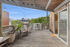 Terraza de madera con mobiliario exterior, una planta en maceta y un ventanal corredero que da a una habitación.