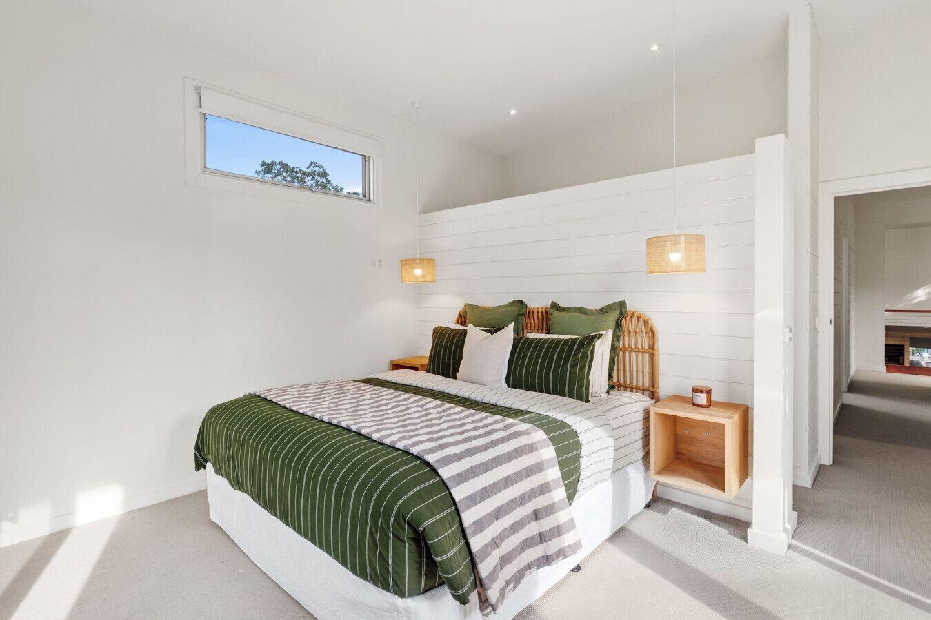 A modern bedroom with a large bed, two bedside tables, a small window, and a view of a staircase.