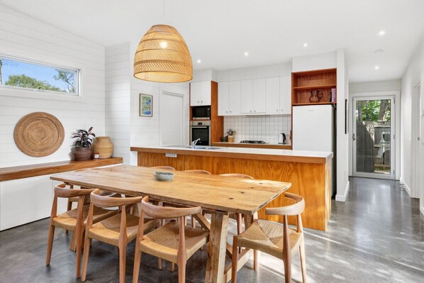 Cocina moderna con una mesa y sillas de madera, una lámpara colgante y vistas al exterior.