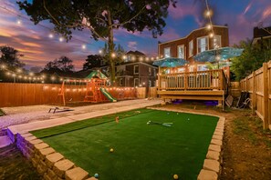 Un patio trasero con un parque infantil, una terraza y una mesa de billar.