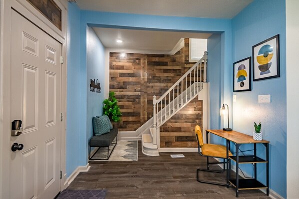 A hallway with a wooden wall, a staircase, a bench, a table with a plant, and framed artwork on the wall.