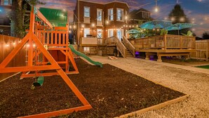 Un jardin avec une structure de jeux en bois, un patio couvert et une maison en arrière-plan.