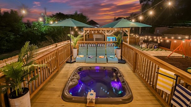 Une terrasse en bois avec un jacuzzi, des chaises longues et des parasols.