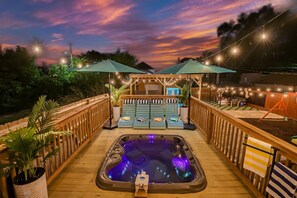 Una terraza de madera con un jacuzzi, sillas de descanso y sombrillas.