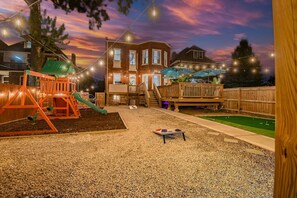 Un patio trasero con un parque infantil, una terraza y una pequeña mesa.