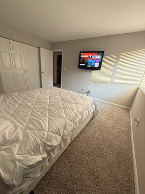 Ein Schlafzimmer mit einem Bett, einem an der Wand montierten Fernseher und einem Kleiderschrank.