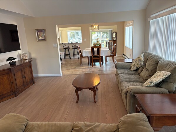 A living room with a sofa, a coffee table, a TV, and a dining area with chairs and a table.